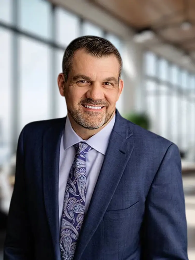 A photo of health care litigation specialist attorney Tommy Hastings in a suit and tie, standing in a professional office building.